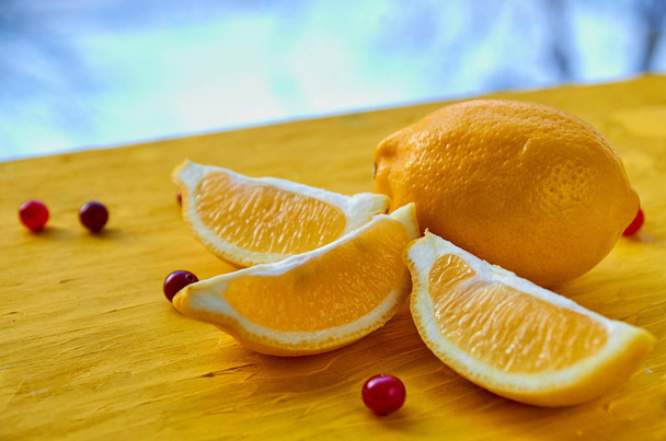 Lemons slices and cranberry on bright yellow wooden table close up. Citrus on the blurred nature background. Side view - Photo, Image