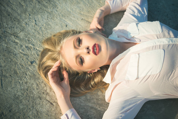 Beauty, look concept. Sensual woman with red sexy lips on makeup face outdoor. Haircare, health, hairstyle. Skincare, skin, make up. Girl with long blond healthy hair lie on concrete surface. - Foto, afbeelding