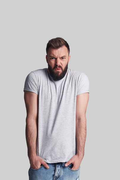 Angry young man looking at camera and standing against grey background - Photo, image