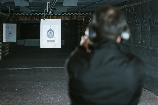 вид сзади человека, нацеливающего пистолет на мишень в тире
 - Фото, изображение