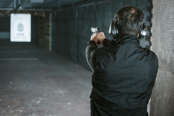 Mann zielt mit Waffe auf Scheibe im Schießstand - Foto, Bild