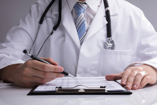 Primer plano de la mano de un médico analizando el informe en el escritorio blanco
 - Foto, Imagen