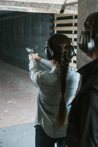 rear view of girl shooting with gun in shooting range - Photo, Image