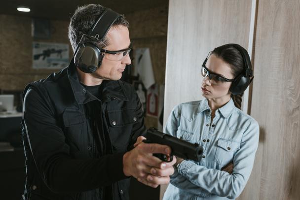 mannelijke instructeur beschrijven pistool naar vrouwelijke client in de schiettent - Foto, afbeelding