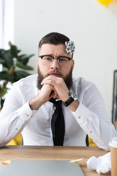 Portret van doordachte zakenman met strik op hoofd op werkplek op kantoor - Foto, afbeelding