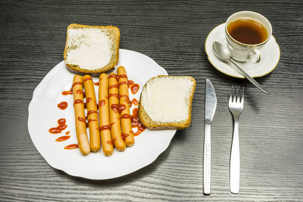 Egy tányér főtt kolbász, egy csésze forró teát, és ketchup. - Fotó, kép