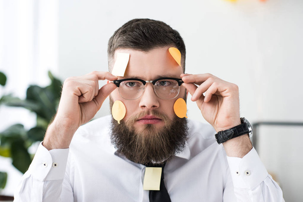 портрет бизнесмена в очках с липкими нотами на лице в офисе
 - Фото, изображение