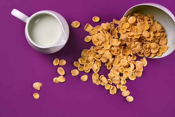 Чаша с кукурузными хлопьями, кувшин молока на фиолетовом фоне, вид сверху
 - Фото, изображение
