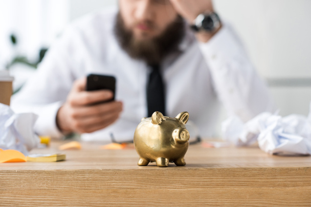 selective focus of piggy bank and businessman with smartphone - Photo, Image