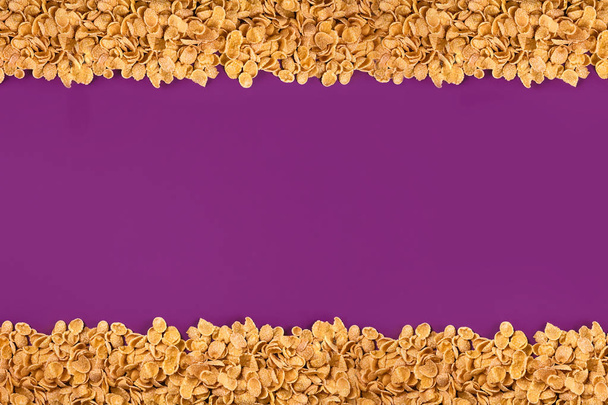 Un cadre doublé de flocons de maïs. Cornflakes dispersés sur un fond violet. Espace de copie
 - Photo, image