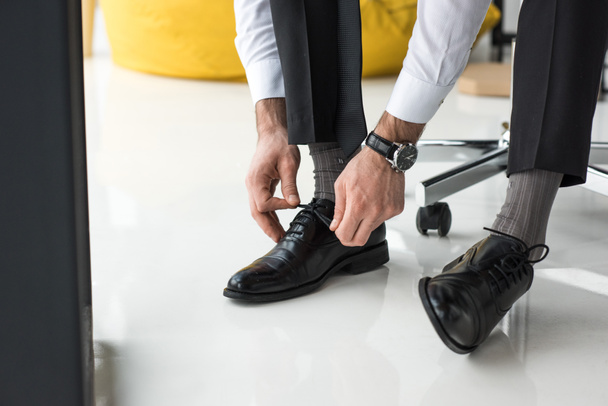 partial view of businessman tying shoelaces in office - Foto, imagen