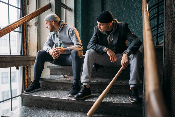 Két férfi rablók lépcsőn ül. Utcai banditák, baseball denevér és az alkohol várakozás áldozat bűncselekmény fogalma - Fotó, kép