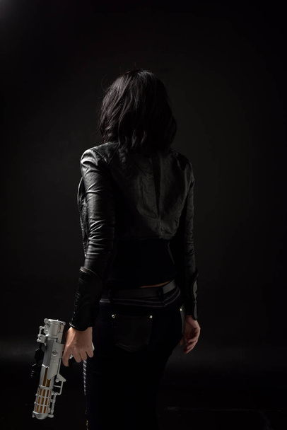 πορτρέτο του μαύρα μαλλιά κορίτσι φορώντας δερμάτινα ρούχα, κυκλοθυμική φωτισμού σε μαύρο φόντο. - Φωτογραφία, εικόνα