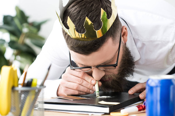 biznesmen z papieru korony na głowie biorąc narkotyki w miejscu pracy w biurze - Zdjęcie, obraz