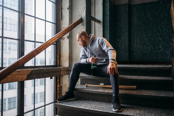 male theif with bottle of alcohol sitting on stairs waiting for victim, crime concept - Fotoğraf, Görsel