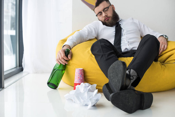 drunk businessman in formal wear with bottle of champagne sleeping on bag chair - Foto, Bild