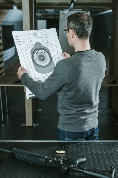 вид сзади стрелка, смотрящего на использованную мишень после стрельбы на стрельбище
 - Фото, изображение