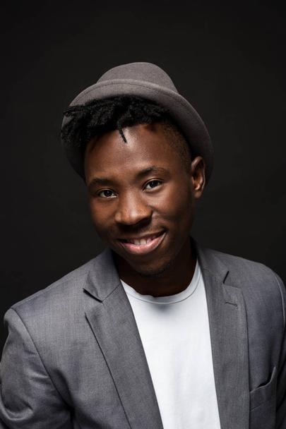 安っぽい帽子魅力的な若い黒人男性スタジオの肖像画が暗い背景に笑顔します。 - 写真・画像