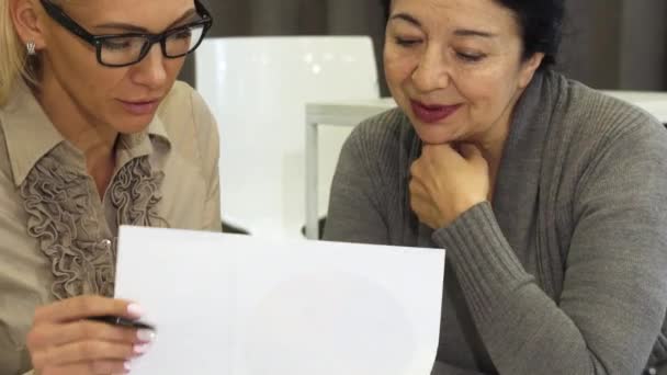 Close up de duas mulheres de negócios discutindo papéis no escritório
 - Filmagem, Vídeo
