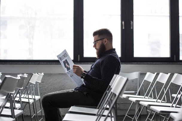 вид збоку зосереджений бізнесмен читає газету, сидячи в кімнаті для переговорів
 - Фото, зображення
