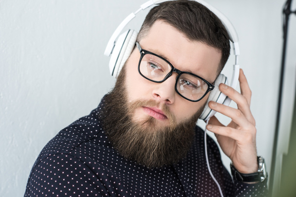portrait of pensive bearded man in eyeglasses listen music in headphones - Фото, изображение