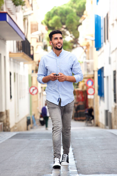 Portrait complet de jeune homme arabe marchant en ville avec téléphone portable et écouteurs
 - Photo, image
