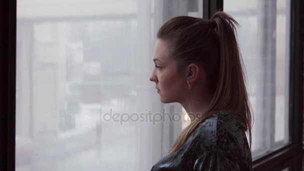 Ongelukkige jonge vrouw kijkt uit het raam - Video