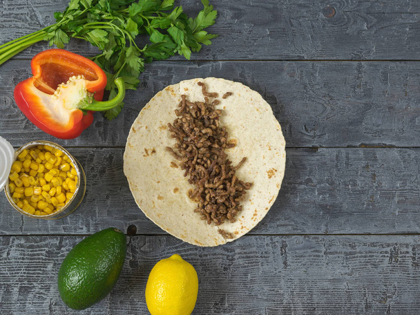 Dort z kukuřičné mouky s mletým hovězím na dřevěný stůl a ingredience pro mexické tacos. Jídlo mexické kuchyně. - Fotografie, Obrázek