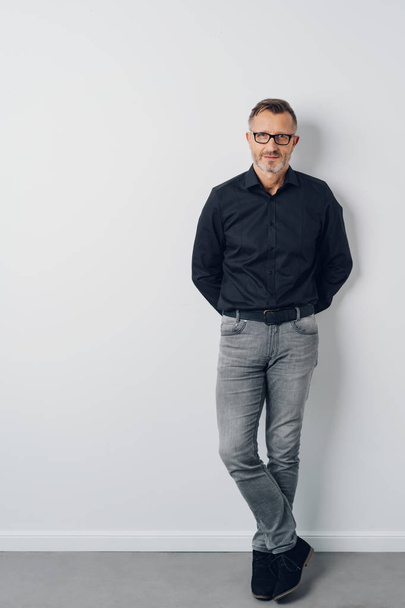 Full length studio shot portrait of a middle-aged confident man wearing cool casual clothes while looking at camera against gray background for copy space - Fotoğraf, Görsel