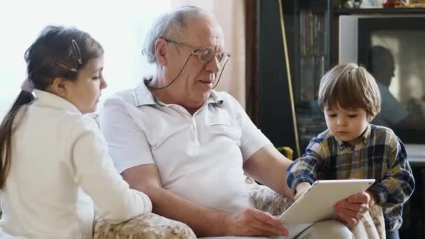 Vanhempi mies, joka käyttää taulutietokonetta lapsenlasten kanssa.
 - Materiaali, video