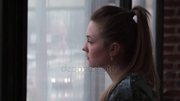 Nahaufnahme einer jungen, traurigen Frau, die aus dem Fenster schaut - Filmmaterial, Video
