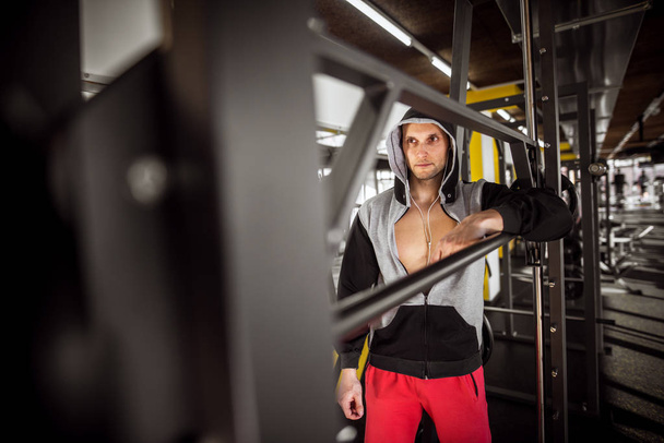muscular hooded man standing with earphones in gym - 写真・画像