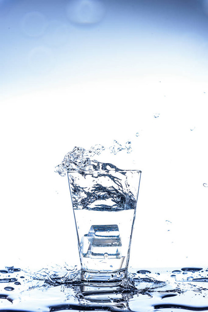 Jég, csepegtető, és fröccsenő tükörképe a pohárban a víz - Fotó, kép