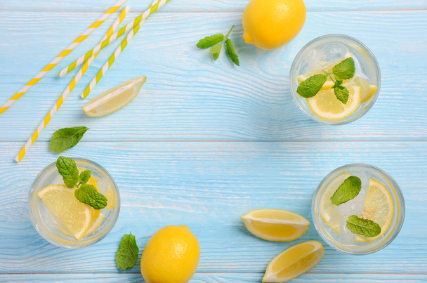 Cold refreshing summer drink with lemon and mint on light blue wooden background, top view, flat lay, copy space. - Fotó, kép