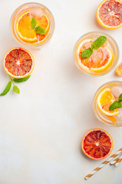 Холодный освежающий напиток с кровью апельсиновых ломтиков в стакане на белом бетонном фоне. Вид сверху, плоский, копировальное пространство
. - Фото, изображение