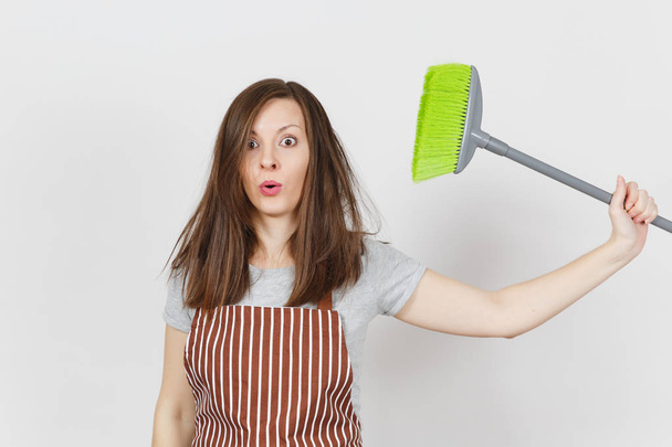 Young fun crazy dizzy loony wild tired shocked housewife with tousled hair in striped apron isolated on white background. Mad witch woman holding broom from the side. Copy space for advertisement. - Φωτογραφία, εικόνα