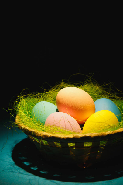 Colorido pastel monofônico tradicional pintado ovos de Páscoa em cesta com grama verde no fundo azul escuro com sombras pretas, silhueta, luz. Espaço de cópia para propaganda. Com lugar para texto
 - Foto, Imagem