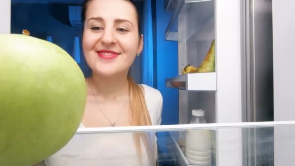 4k vídeo de bela mulher sorridente olhando em prateleiras do refrigerador e mordendo maçã verde
 - Filmagem, Vídeo