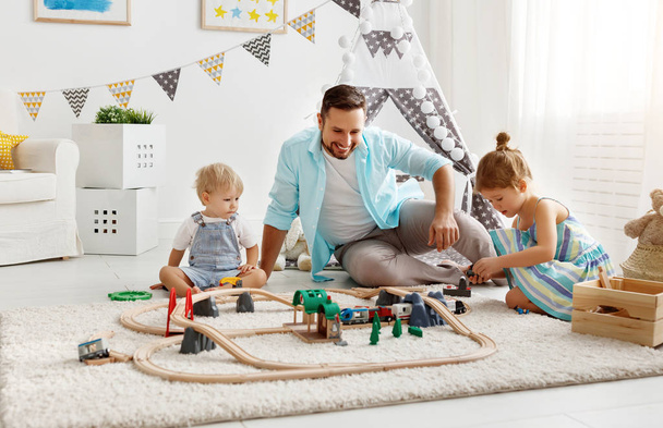 отец и дети играют в игрушечную железную дорогу в игровой комнате
 - Фото, изображение