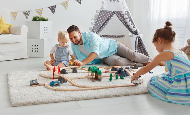 батько сім'ї і діти грають в іграшкову залізницю в ігровій кімнаті
 - Фото, зображення