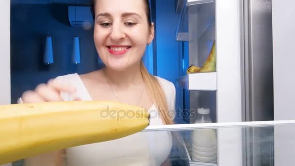 4k кадров, где молодая улыбающаяся женщина берет банан из холодильника, чистит и кусает его
 - Кадры, видео