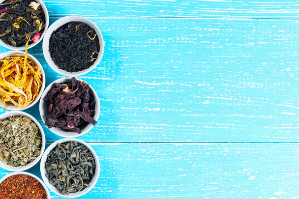 Различные сушеные лекарственные травы и чаи в нескольких мисках на синем деревянном фоне
 - Фото, изображение