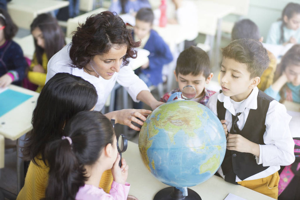 женщины-учителя и студенты смотрят на земной шар с увеличением
  - Фото, изображение