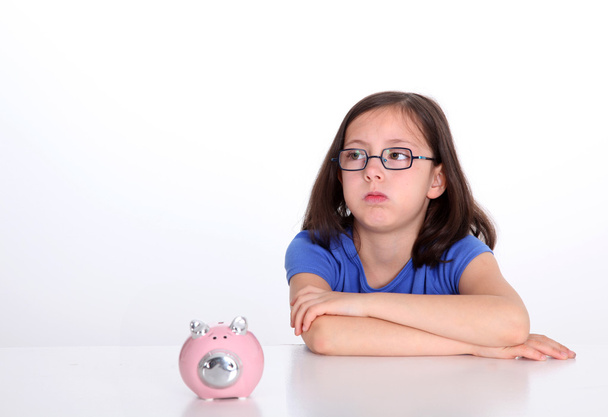 Little girl with bored look sitting by piggybank - 写真・画像