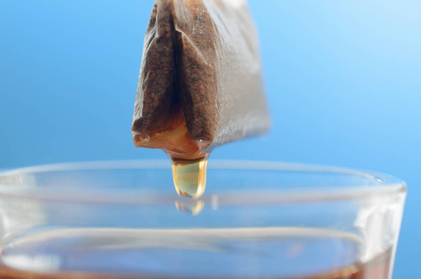 Um saco de chá sobre uma caneca de vidro com água quente close-up em um fundo azul
. - Foto, Imagem