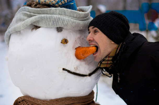 Happy man sculpt a big real snowman. Funny man has fun in winter park, wintertime - Photo, Image
