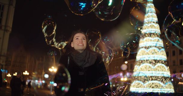 Beautiful girl having fun among big soap bubbles in a city at night. - Foto, imagen