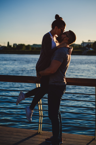 Hombre sosteniendo y besando a su novia en un atardecer
 - Foto, Imagen