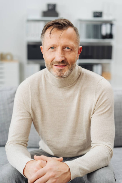 Attractive middle-aged man with an earnest expression sitting at home on a sofa staring intently at the camera - Foto, Bild