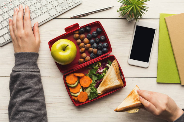 Woman eating healthy sandwich from lunch box at her working table - Photo, Image